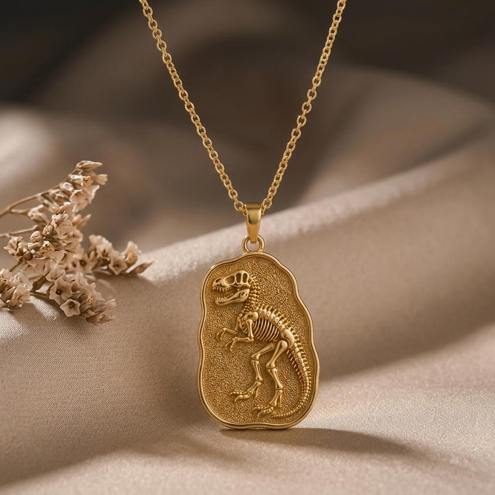 Gold Plated Silver Albertosaurus fossil pendant with raised dinosaur skeleton on textured plaque over beige satin beside dried flowers