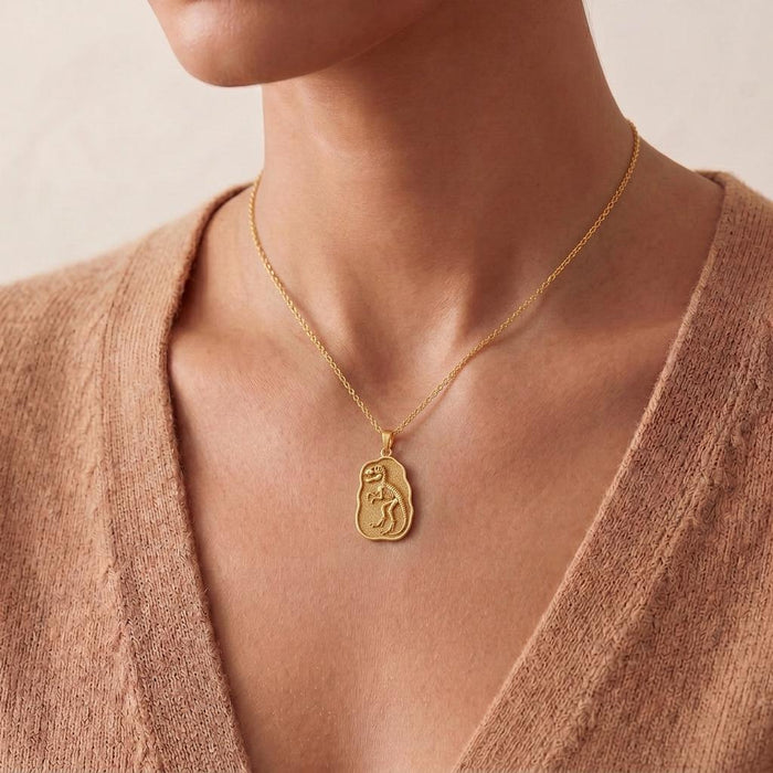 Close worn view of Gold Plated Silver Albertosaurus fossil pendant on a textured plaque against a beige V-neck knit top