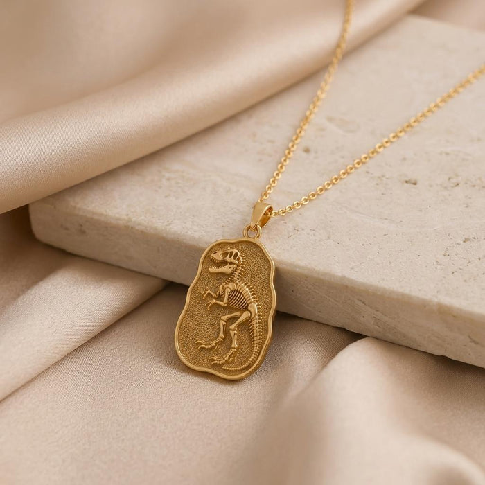 Gold Plated Silver Albertosaurus fossil pendant with raised dinosaur skeleton displayed on a stone slab and beige satin