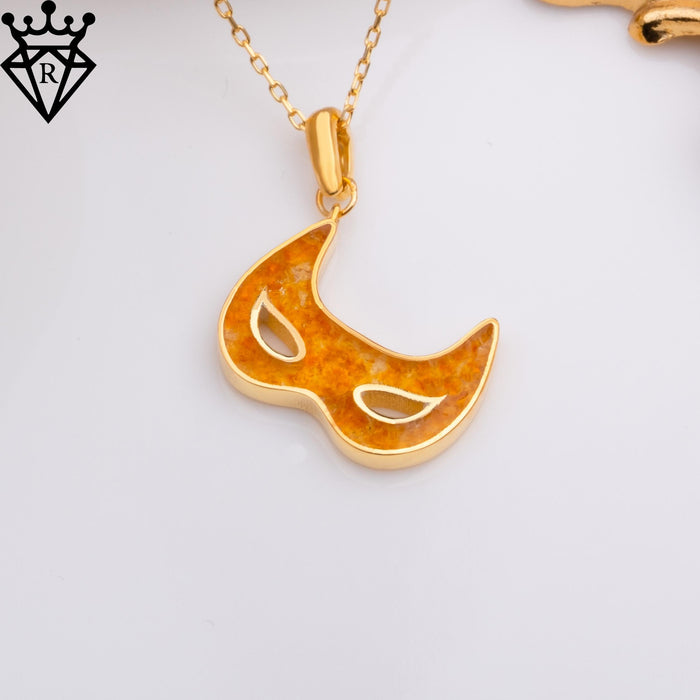Amber-toned Venetian mask pendant on a chain against a white background with a black crown-and-diamond logo watermark in the upper-left corner