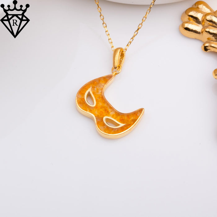 Amber-toned Venetian mask pendant beside gold-toned decorative objects with a black crown-and-diamond logo watermark