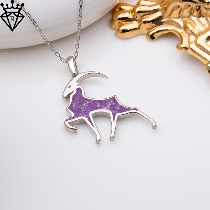 Angled view of the goat necklace beside a white dish, showing the outstretched legs