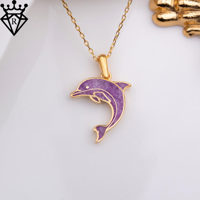 Overhead view of the leaping dolphin necklace beside a gold decorative prop and white dish