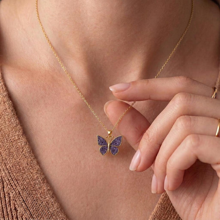 Gold Plated Silver butterfly necklace worn at the neckline with a hand beside the textured purple pendant