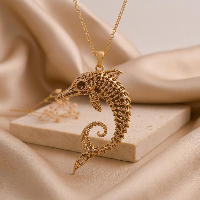 Gold Plated Silver Ancient Dolphin Fossil Necklace with openwork skeletal detailing on satin beside a stone display block