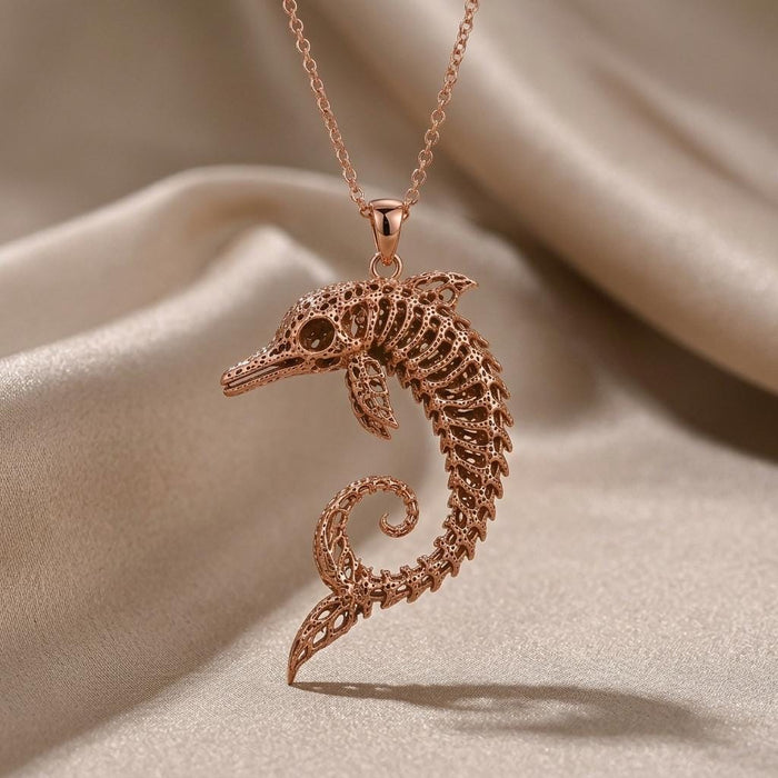 Rose-toned curled skeletal dolphin pendant close-up on draped satin