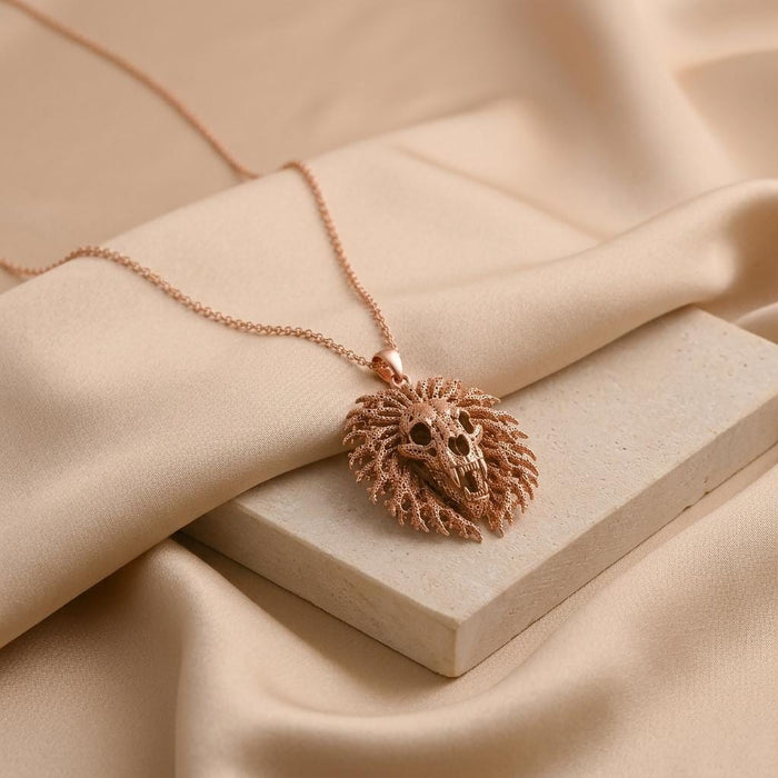 Rose Gold Plated Ancient Lion Skull Crest Necklace displayed on a pale stone block with beige fabric