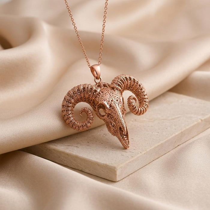 Rose Gold Plated Ancient Ram Skull Pendant on a pale stone slab with champagne fabric