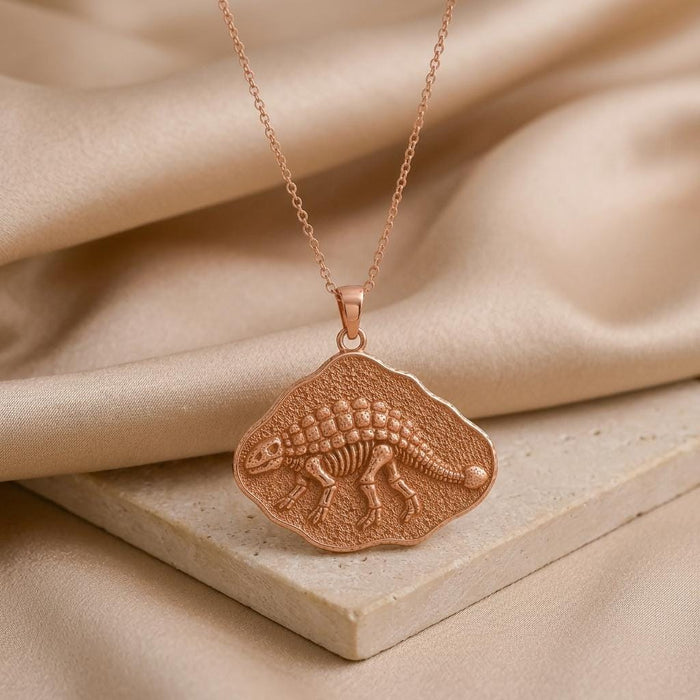 Rose Gold Plated Ankylosaurus fossil pendant necklace on champagne satin beside a stone block