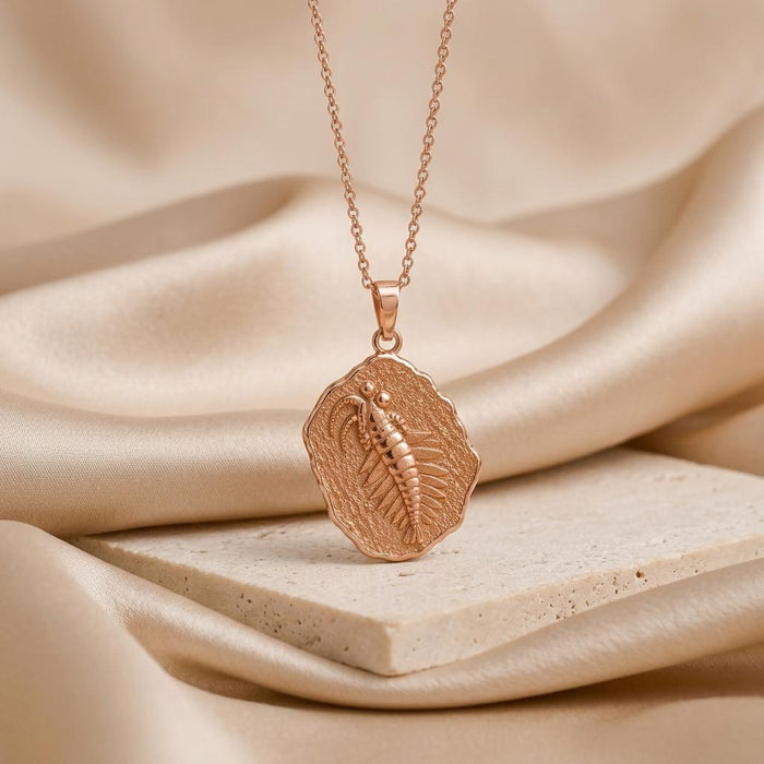 Rose Gold Plated Anomalocaris fossil relief medallion necklace on a pale stone slab and champagne satin