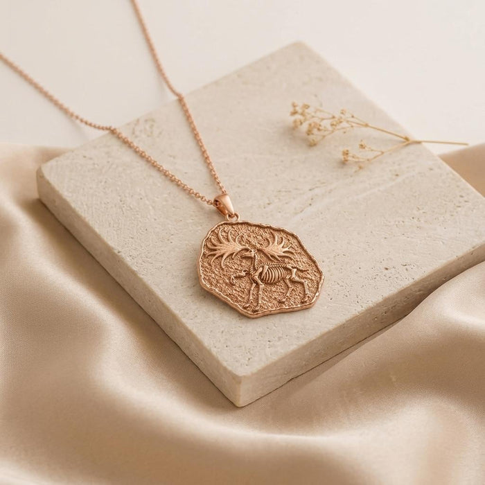 Rose Gold Plated Dire Wolf Fossil Pendant Necklace displayed on a pale stone block and champagne satin