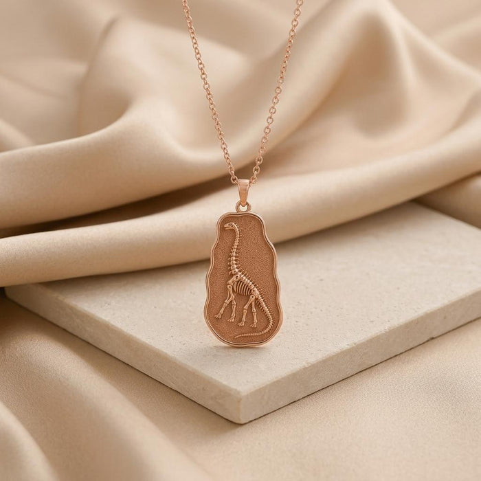 Rose Gold Plated Argentinosaurus fossil pendant necklace with raised skeleton relief on a pale stone slab