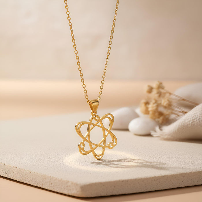 Gold Plated Silver Atom Necklace suspended above a textured beige surface with dried flowers