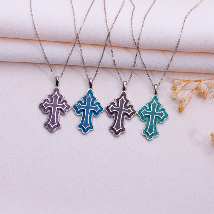 Four scalloped cross pendant necklaces arranged on pale folded fabric