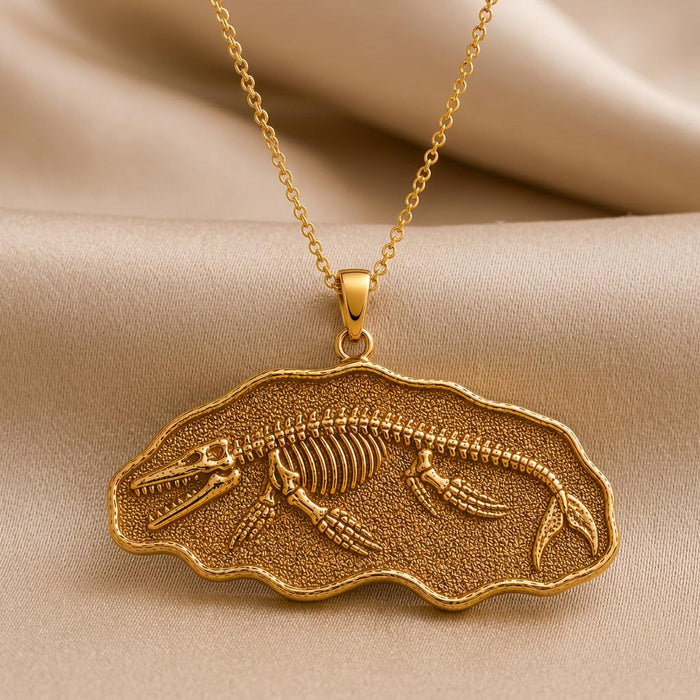 Gold Plated Silver Basilosaurus fossil pendant necklace with a raised skeleton on textured beige fabric