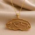 Gold Plated Silver Basilosaurus fossil pendant necklace with a raised skeleton on textured beige fabric