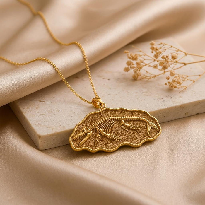 Gold Plated Silver Basilosaurus fossil pendant necklace on a stone block with beige fabric and dried flowers