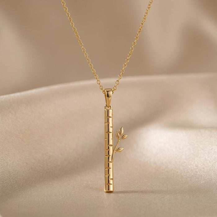 Gold Plated Silver Birch Veil Pendant Necklace with a segmented birch-inspired bar and leafy side branch on beige fabric