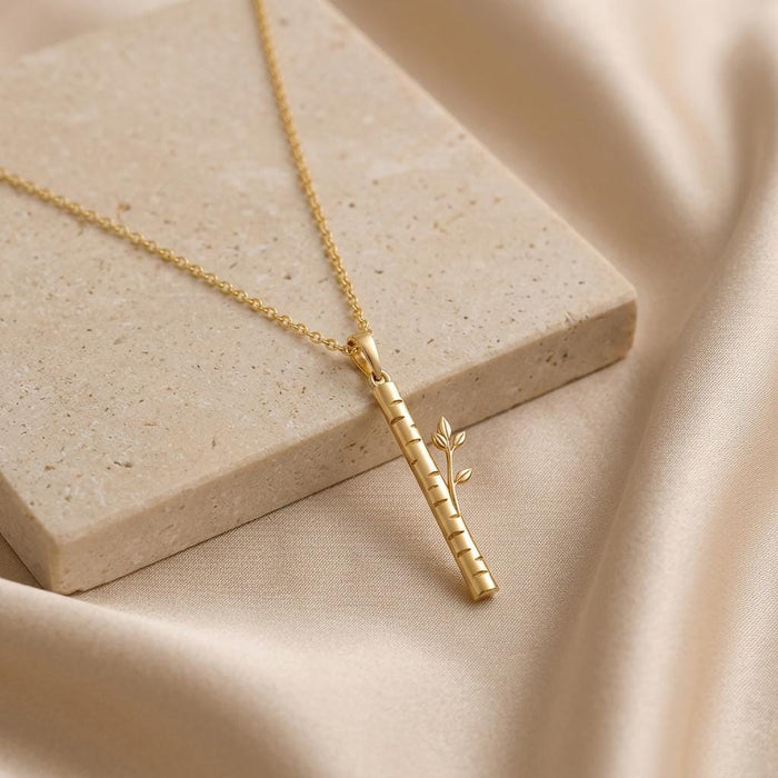 Gold Plated Silver Birch Veil Pendant Necklace resting beside a textured stone block on beige fabric