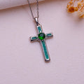 Silver Birthstone Cross Necklace with a green round center stone and green rectangular accents on pale fabric