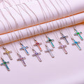 Multiple Birthstone Cross Necklaces with colored arm panels and round center stones arranged on pale pink fabric