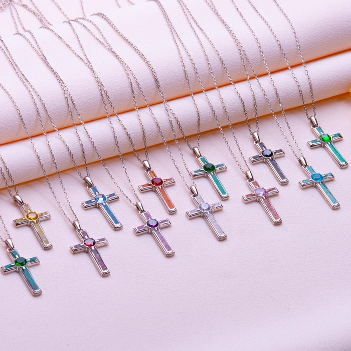 Multiple Birthstone Cross Necklaces with colored arm panels and round center stones arranged on pale pink fabric