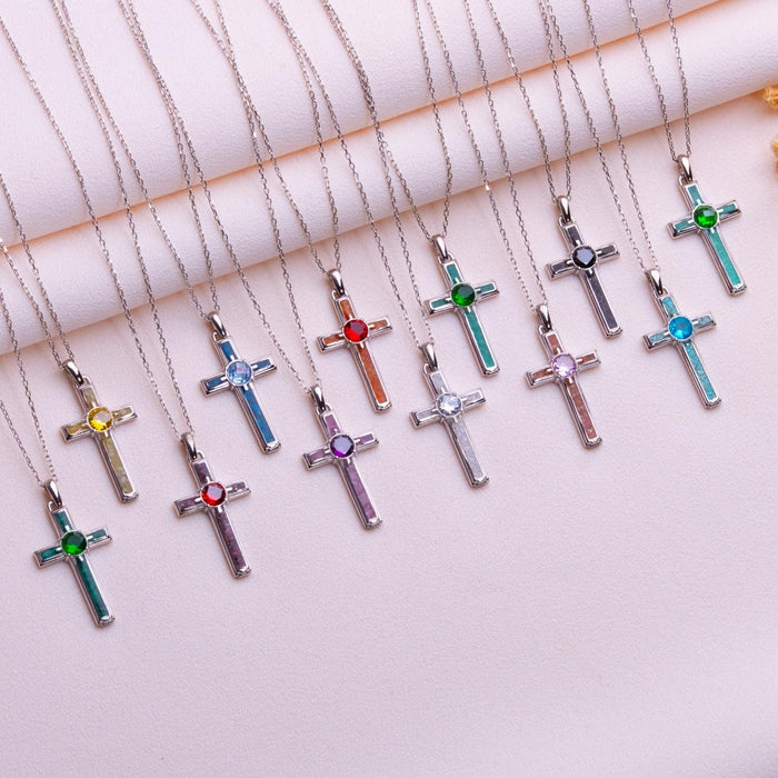 Multiple colored-panel cross necklaces with varied round center-stone colors arranged on pale pink rolled fabric