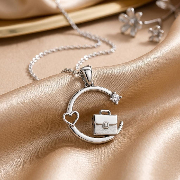 Silver circular briefcase-and-heart pendant with a clear round accent on champagne fabric