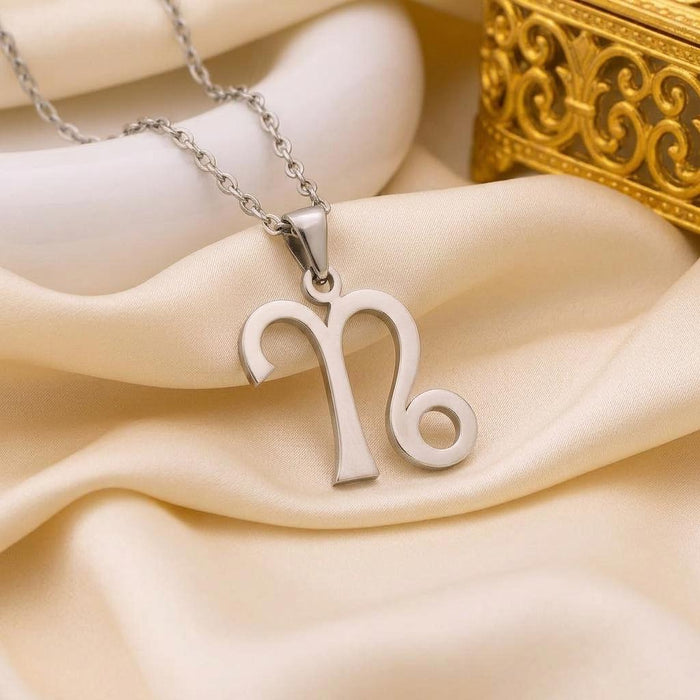 Capricorn glyph necklace arranged on champagne satin beside a decorative gold box