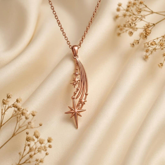 Rose Gold Plated Falling Star Pendant Necklace with curved star trails and a pointed star drop on pale satin