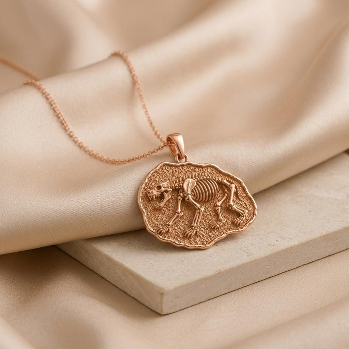 Rose Gold Plated prehistoric bear pendant lying on a pale block beneath draped fabric