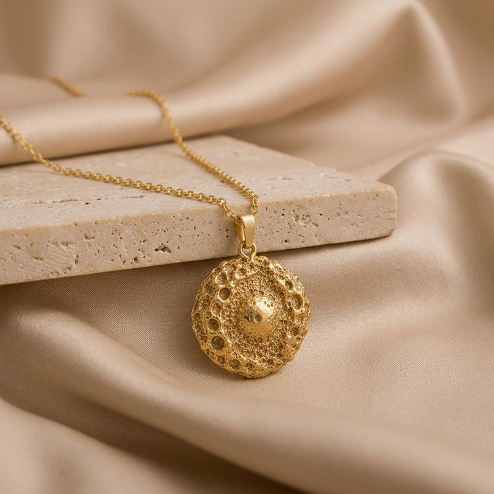 Gold Plated Silver Ceres asteroid pendant necklace beside a pale stone slab on champagne satin