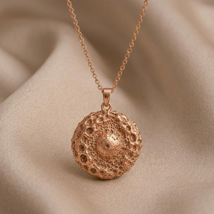 Rose Gold Plated Ceres asteroid pendant necklace with a raised crater-textured center on champagne satin