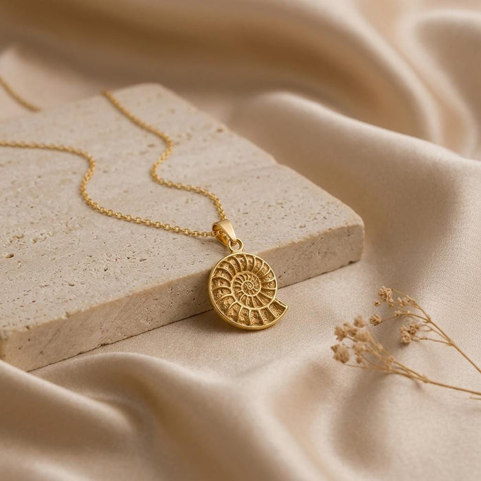 Gold Plated Silver ammonite spiral pendant on a stone block with dried flowers