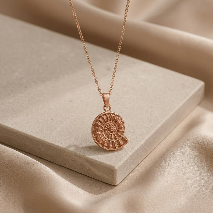 Rose Gold Plated ammonite fossil pendant necklace on a pale stone block