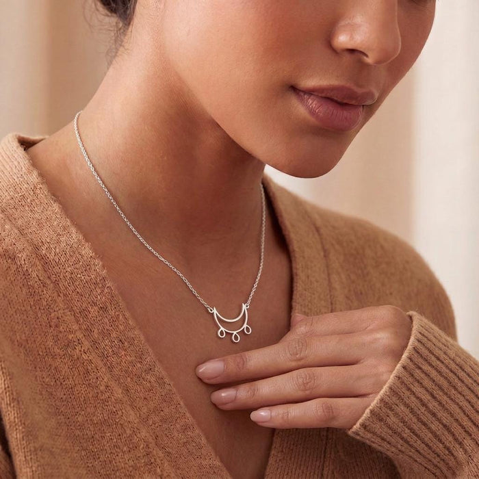 Silver Crescent Moon Necklace with three teardrop dangles worn with a beige knit top