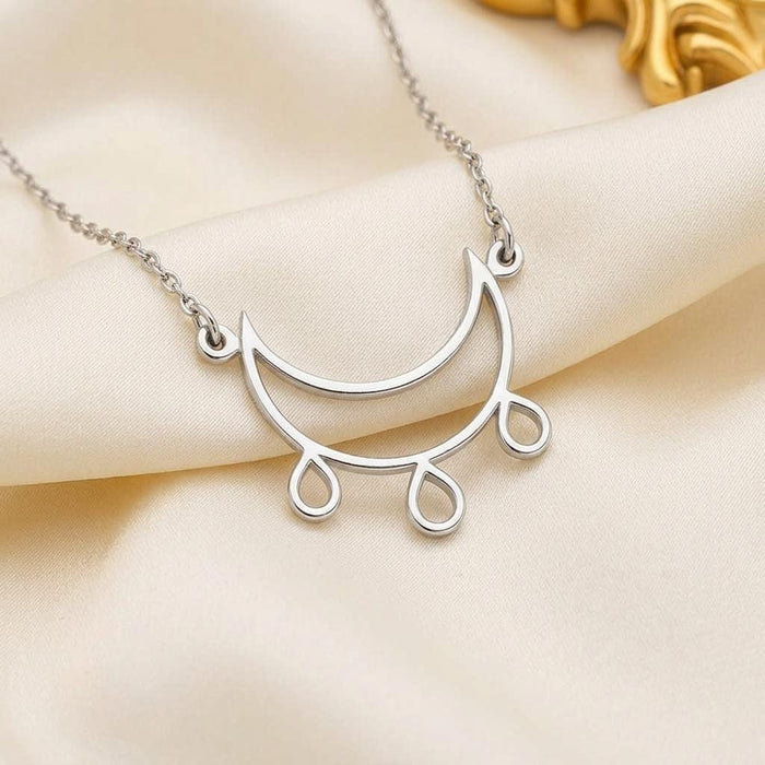 Close-up of a Silver Crescent Moon Necklace with inner curved arc and three teardrop dangles on cream fabric