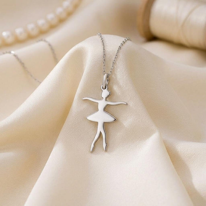 Ballet dancer pendant with outstretched arms displayed on ivory satin beside pearls