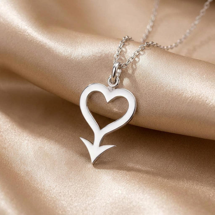 Close-up of the Cupido Symbol Necklace pendant with open heart and arrow detail on satin fabric
