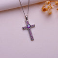 Dainty amethyst cross necklace with rectangular inset panels and a round purple center accent on pale textured fabric