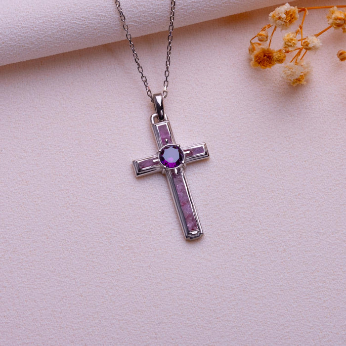 Dainty amethyst cross necklace with rectangular inset panels and a round purple center accent on pale textured fabric