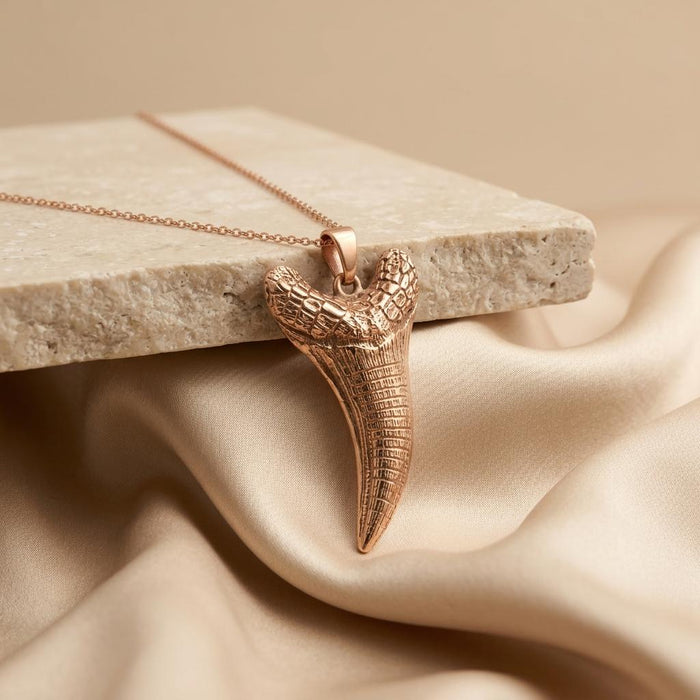 Rose Gold Plated Dakosaurus tooth pendant necklace displayed on stone and champagne satin