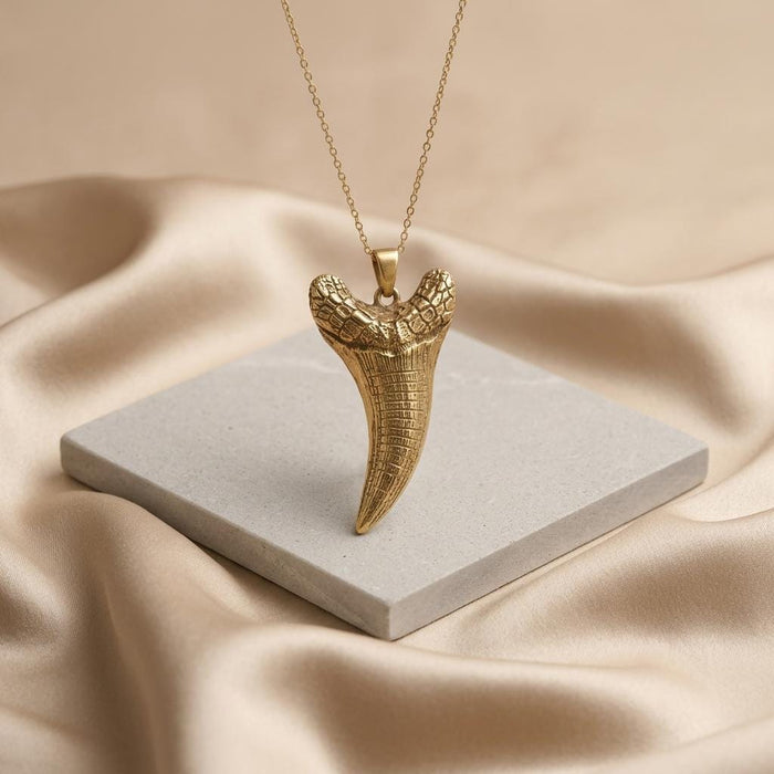 Gold Plated Silver Dakosaurus tooth pendant necklace standing on a square stone tile