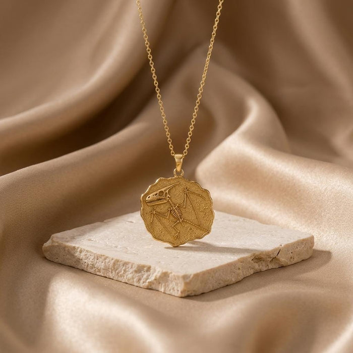 Gold Plated Silver Dimorphodon Fossil Pendant displayed on a pale stone slab over draped satin