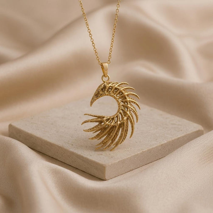 Gold-toned openwork crescent feather pendant hanging above a square stone block on beige fabric