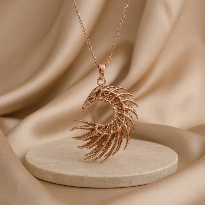 Rose-toned openwork crescent feather pendant displayed above a round stone platform on beige fabric
