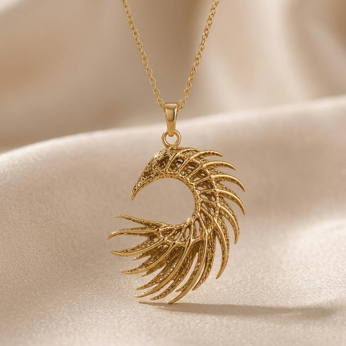 Close-up of a gold-toned openwork crescent feather pendant on beige fabric