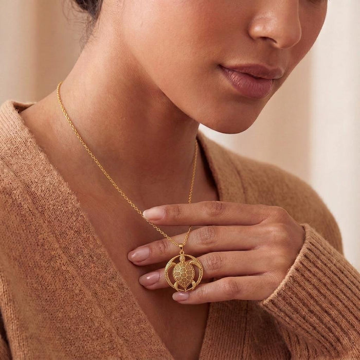 Gold Plated Silver Eclipse Turtle Relic necklace held at the collarbone over a brown knit top