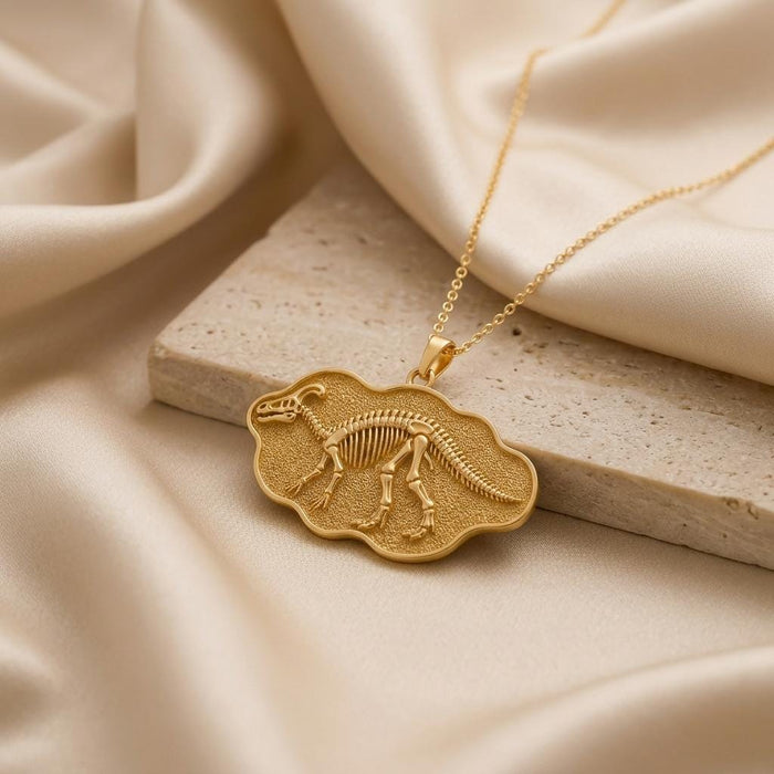 Gold Plated Silver Edmontosaurus fossil pendant with raised skeleton relief on cream satin beside a stone block
