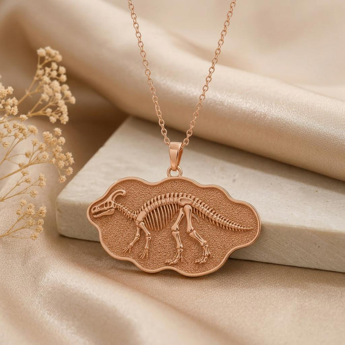 Rose Gold Plated Edmontosaurus skeleton relief pendant on cream satin beside dried flowers